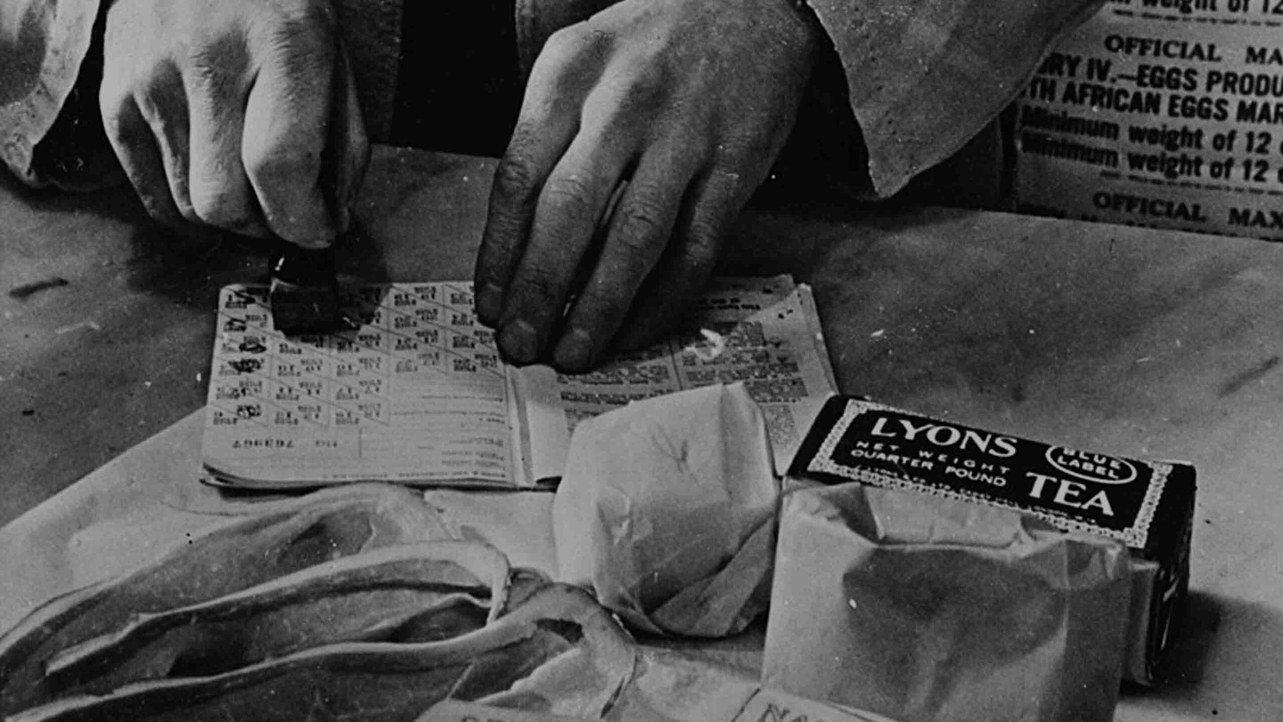 "A British shopkeeper cancels the coupons in a housewife’s ration book for her weekly allowance of tea, sugar, cooking fats, and bacon. April 1943.