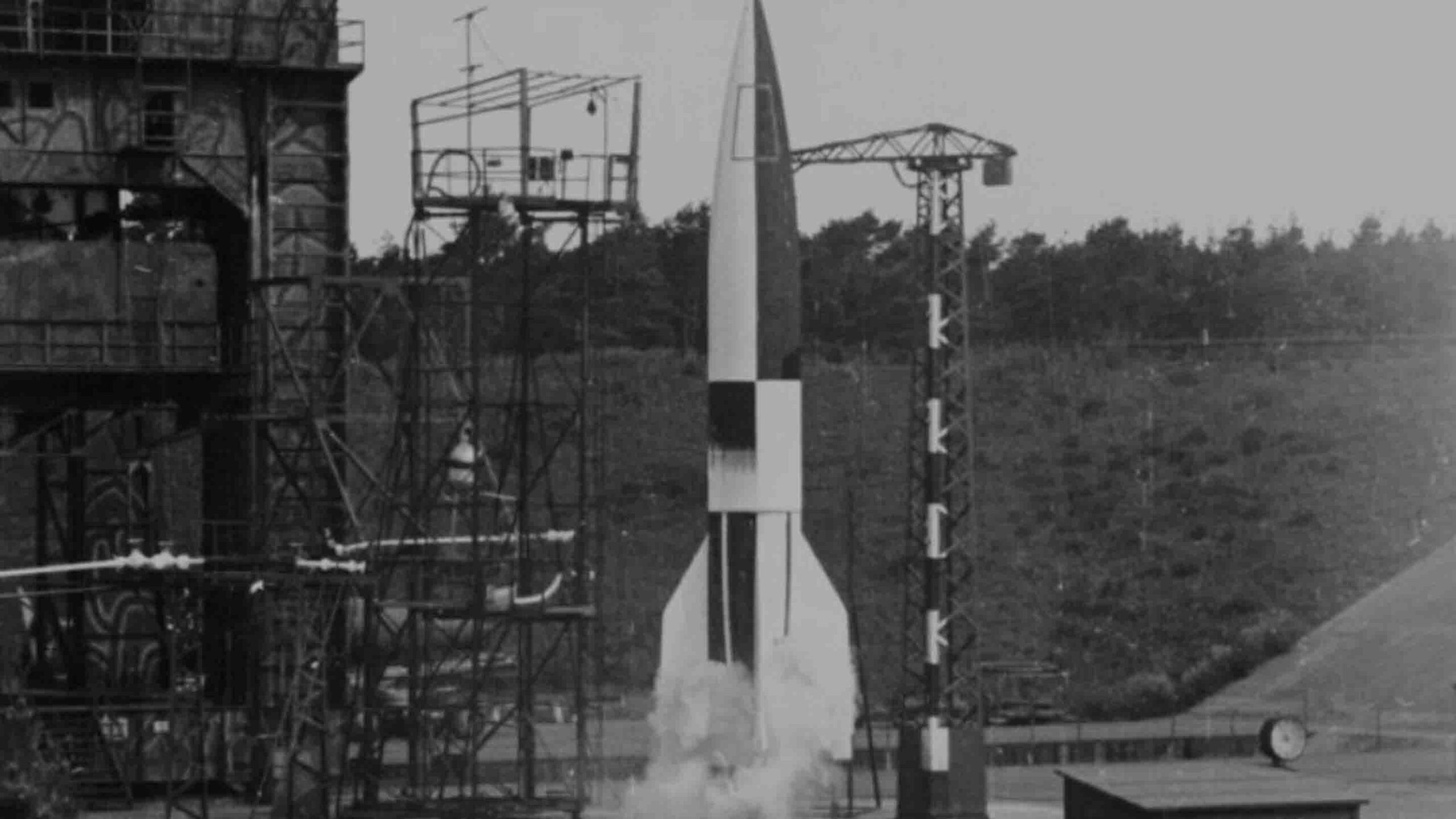 A V-2 rocket launches from the Peenemünde test site, 1943, with a mobile maintenance platform visible on the left.