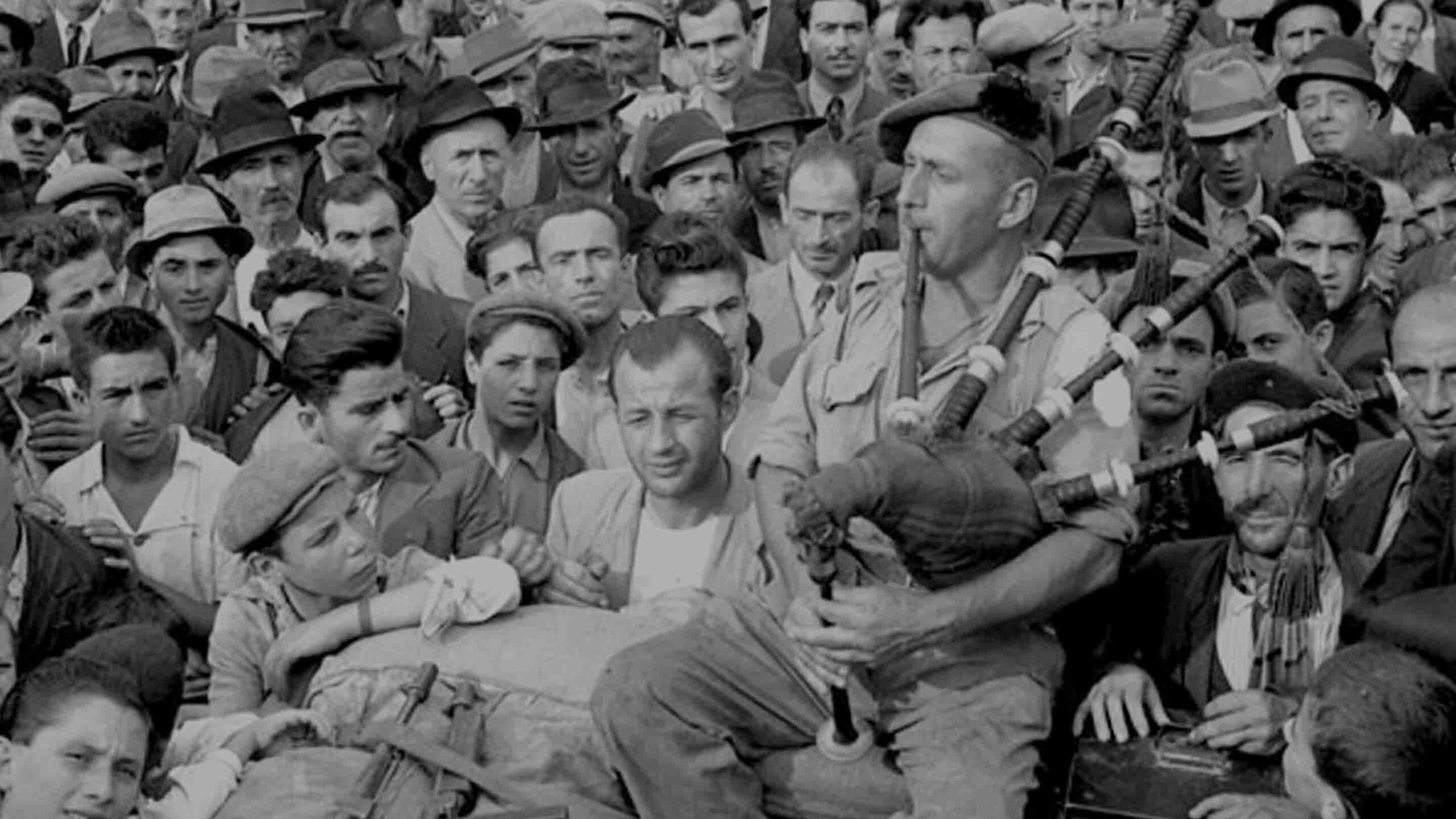 Scottish Piper plays the bagpipes with Italian civilians looking on.
